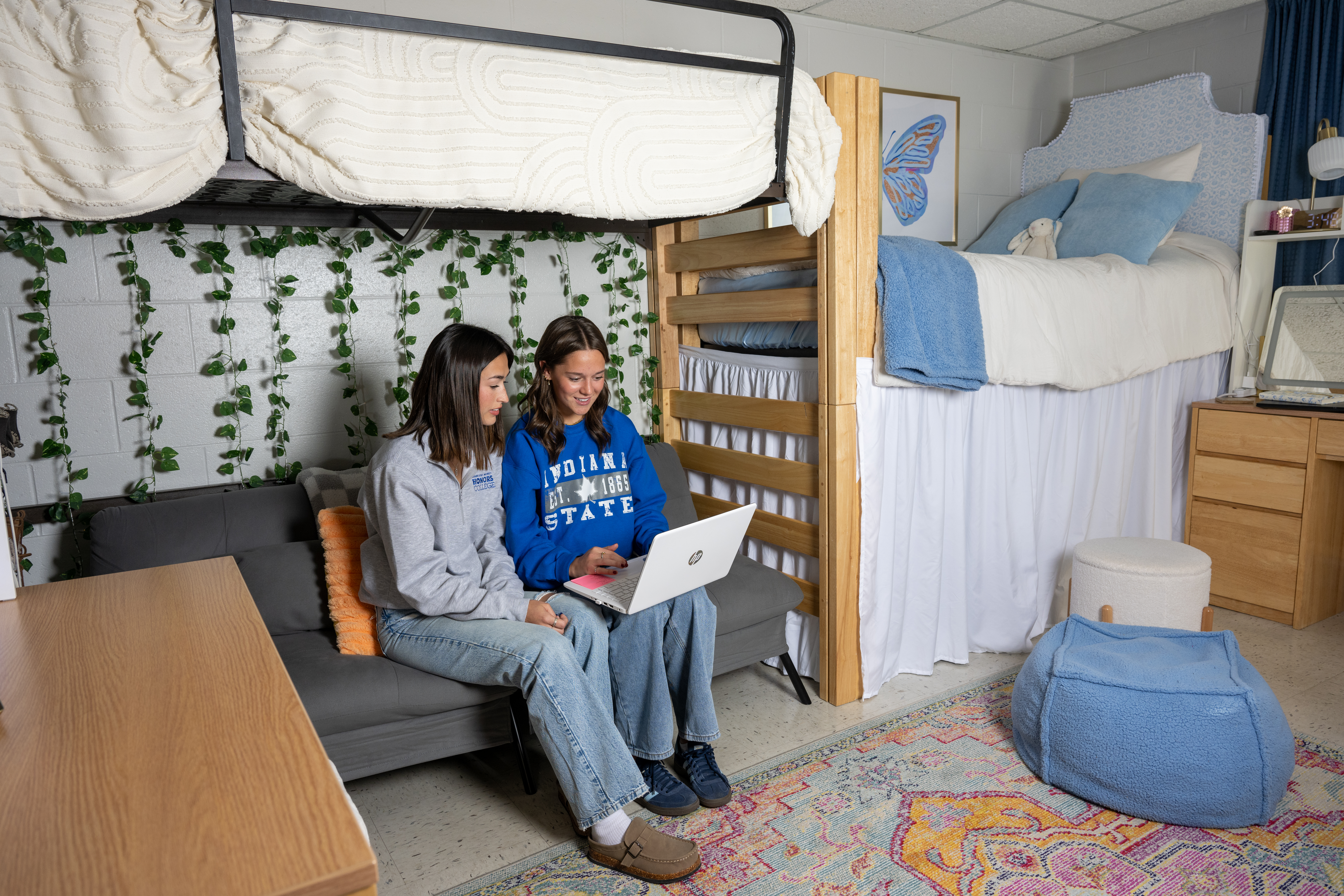 Two Honors students sitting on a couch below a lofted bed in a room in Pickerl Hall. The students are studying together and looking at a laptop.
