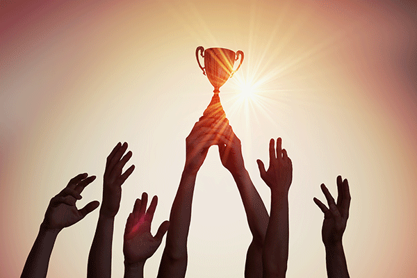 Silhouetted hands raise a trophy against a bright sun, creating a backlit scene with a warm sky in the background.