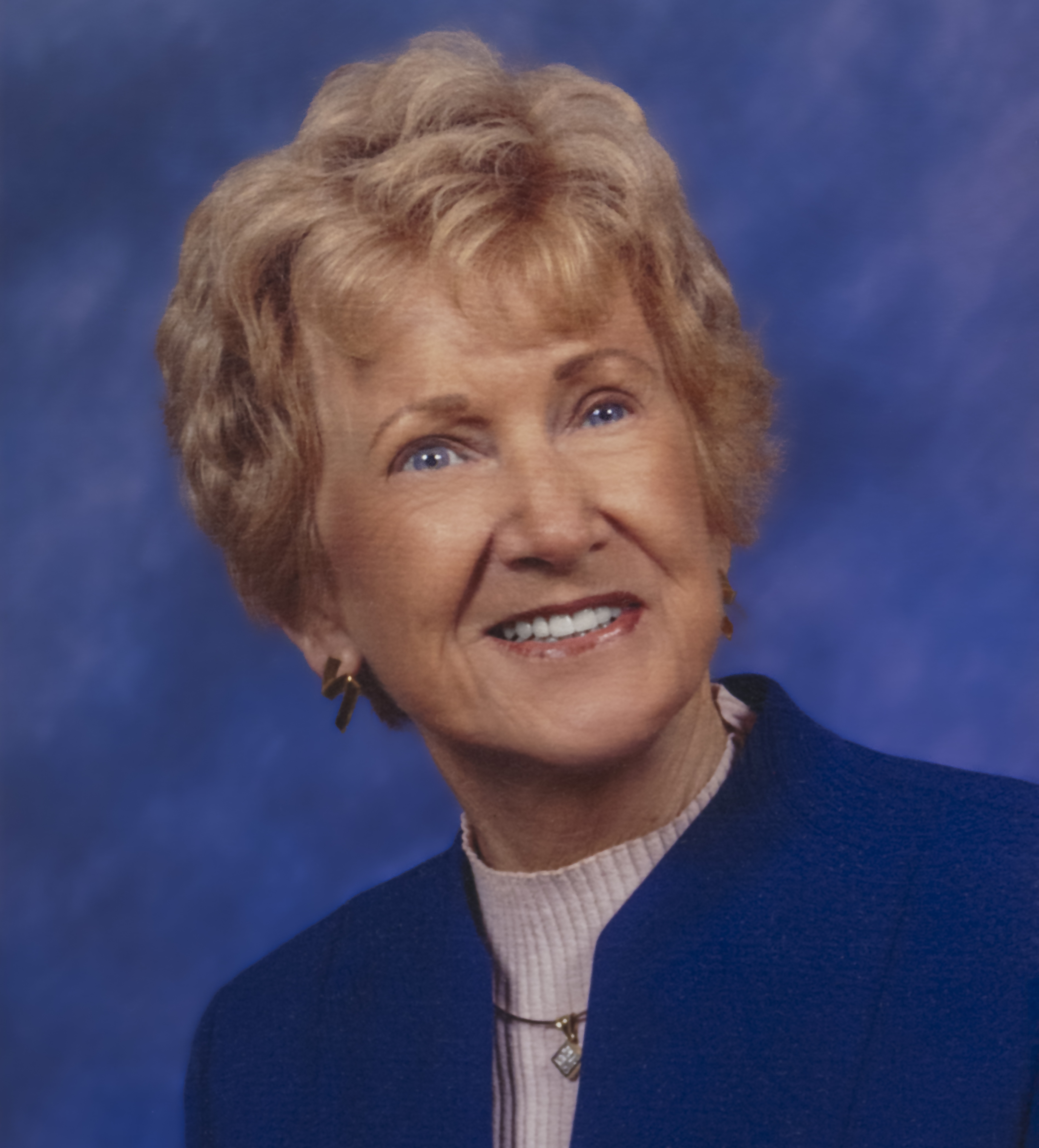 Photo of a woman (Jan McCarthy) in a blue sweater, smiling in front of a blue background. 