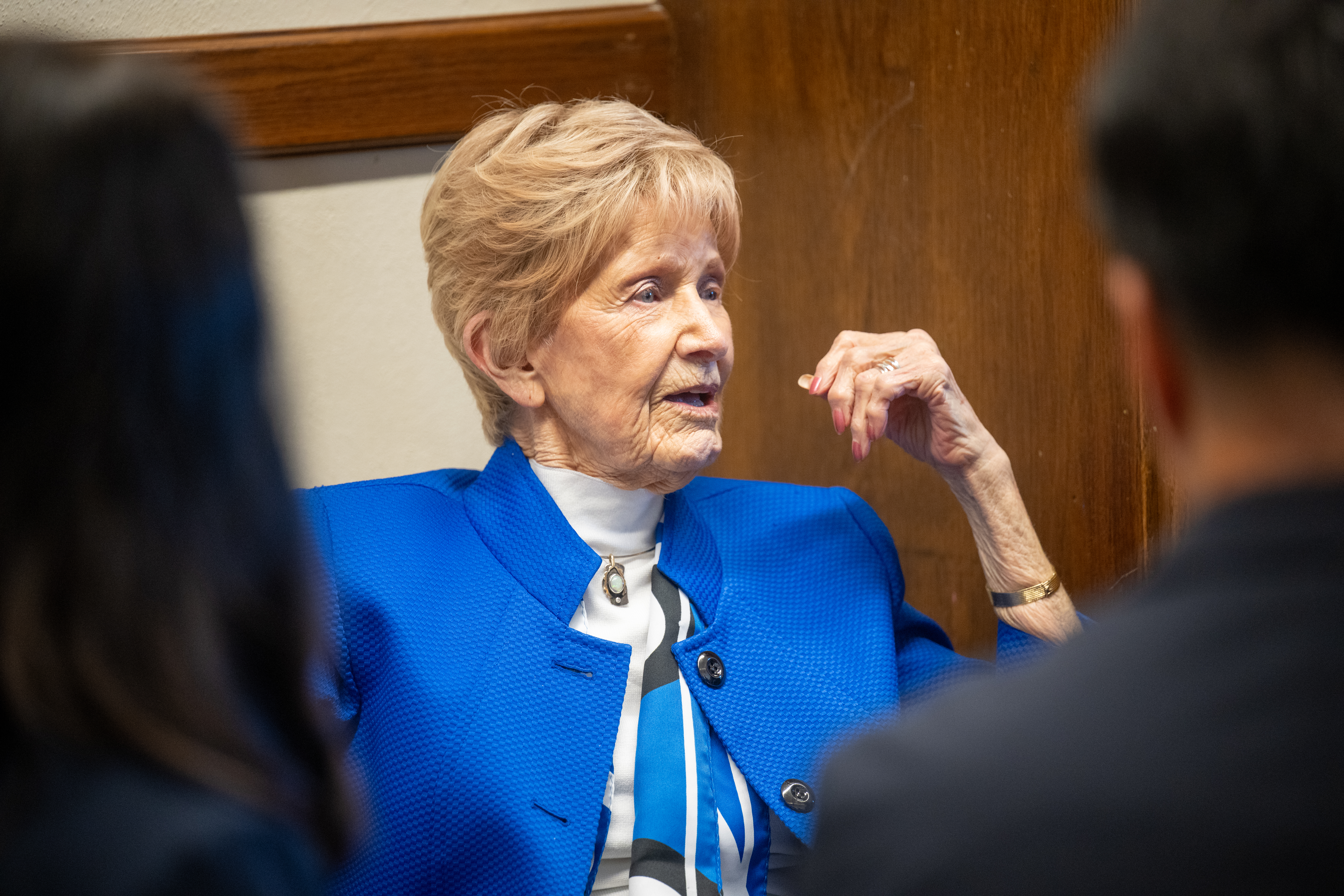 A woman in a blue jacket speaking to a group of people. 