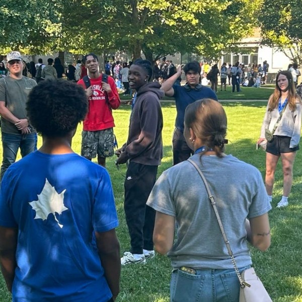 A diverse group of students standing outside in a circle with trees in the background.
