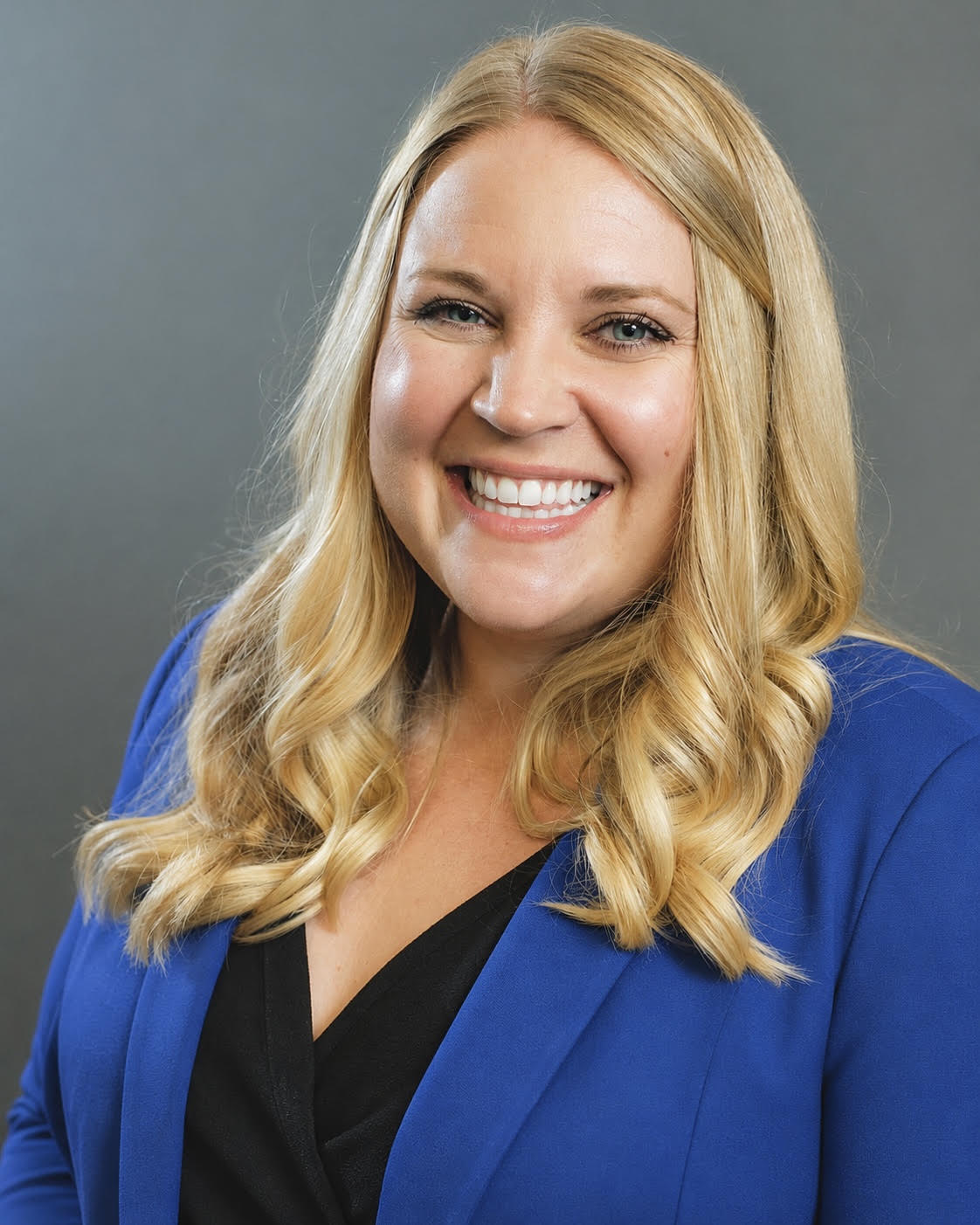 Portrait of Emilee Roberts smiling and wearing a blue blazer against a gray background.