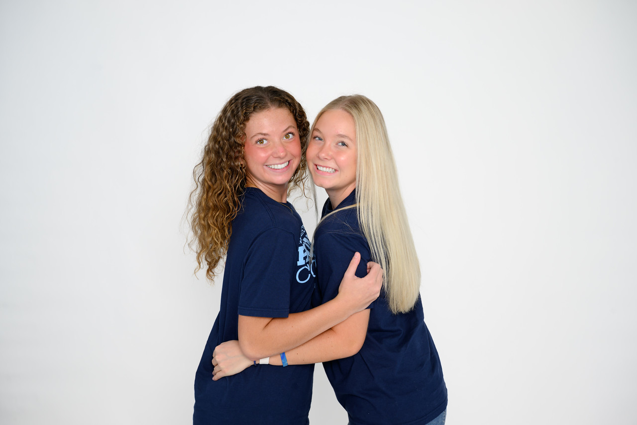 Two young women wearing matching Indiana State University Honors College T-shirts stand together against a plain light-colored studio background. The pair face the camera with their arms around each other in a posed portrait.
