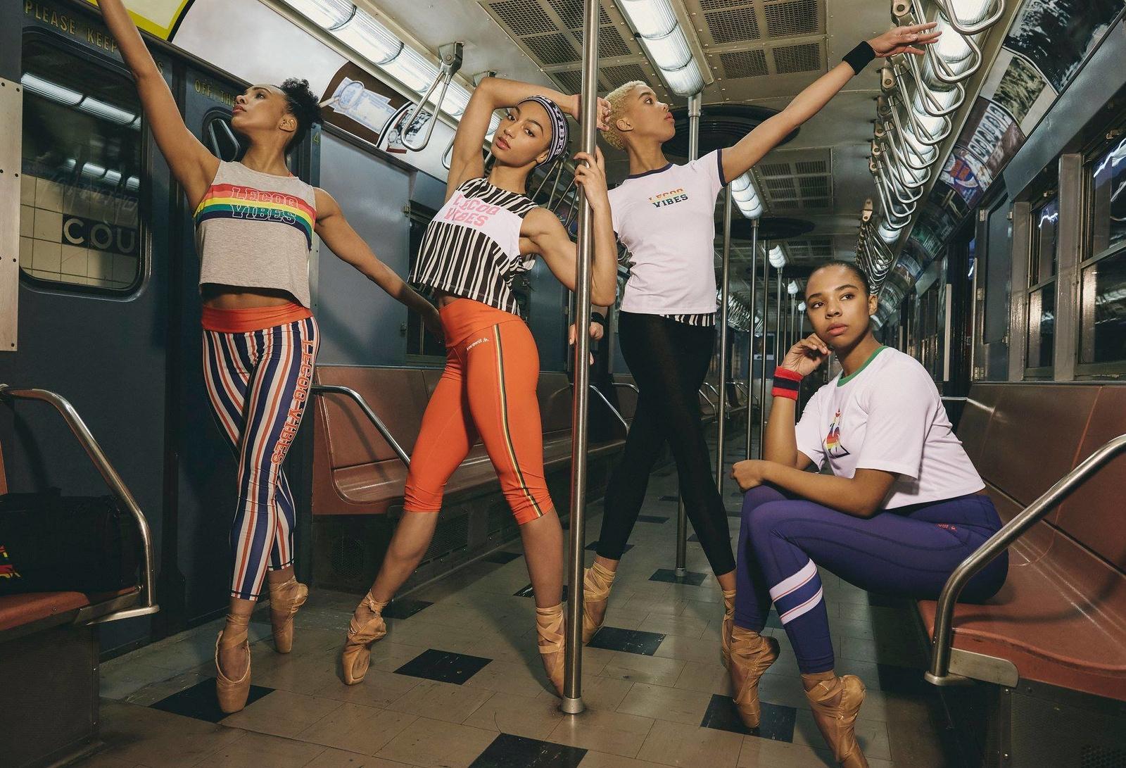 Four female dancers in colorful athletic wear and pointe shoes posing inside a subway car, three standing on tiptoe and one seated.