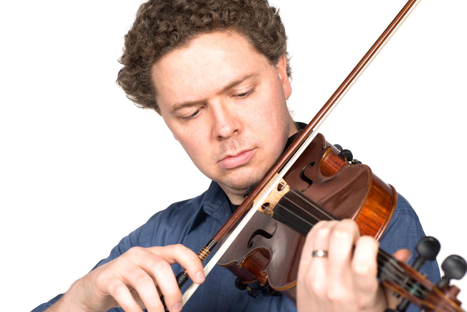 Man with curly hair wearing a blue shirt playing a violin, focusing on the strings and bow against a white background.