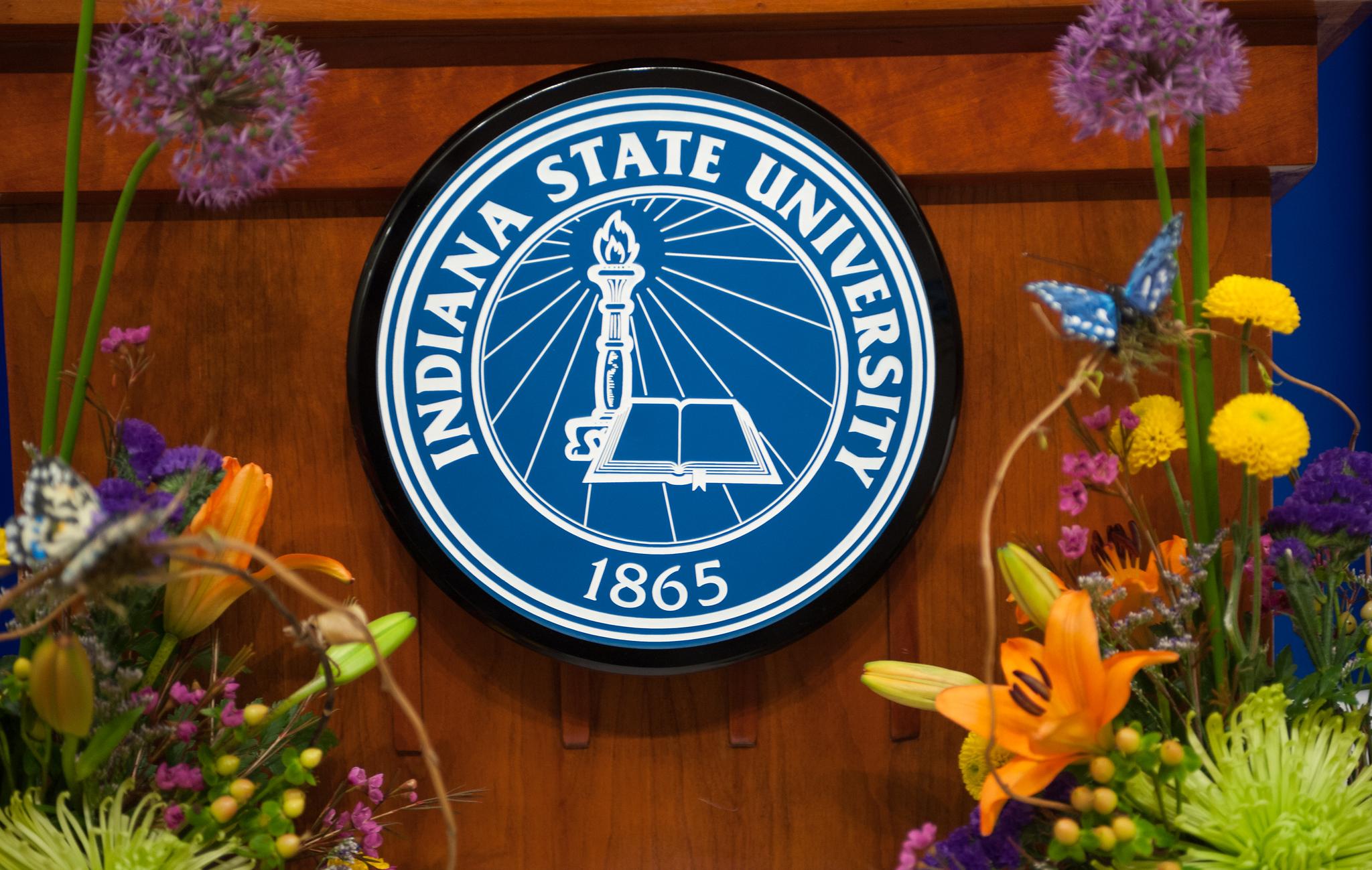 Indiana State University seal on a wooden podium with colorful flowers and butterflies in the foreground.
