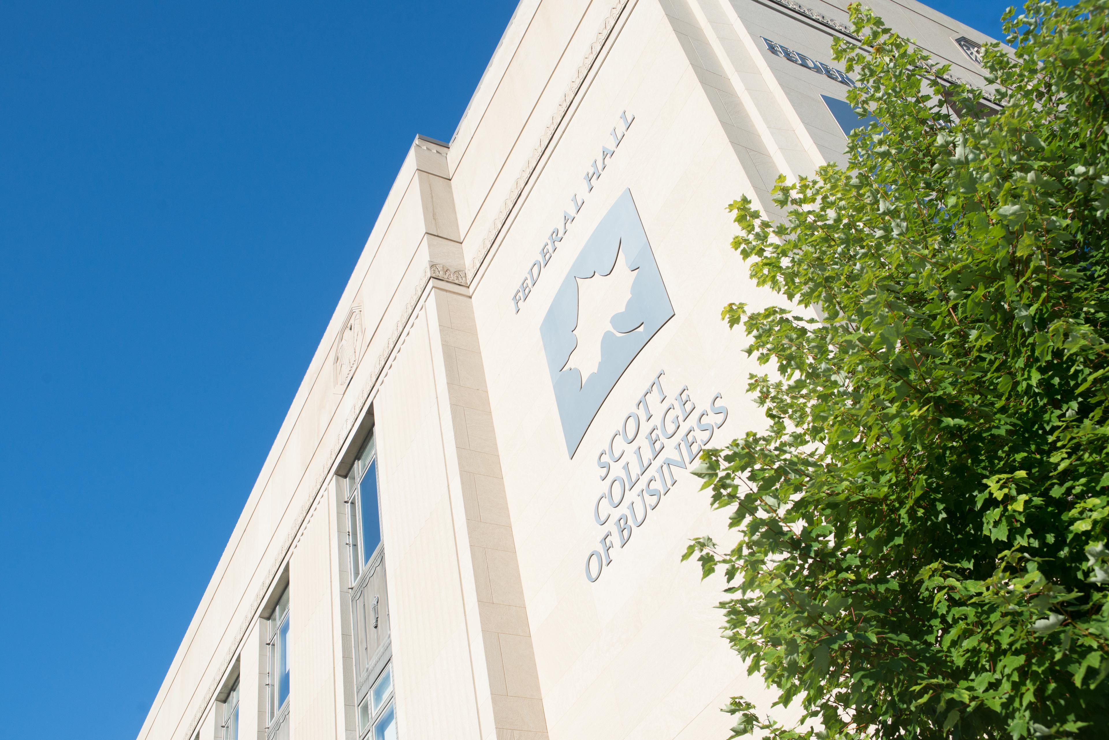 Exterior view of Federal Hall at Scott College of Business with clear blue sky and green tree branches in foreground.
