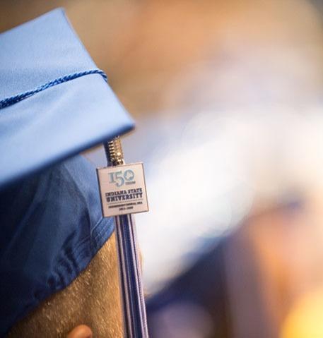 Close-up of a blue and gold graduation cap with a tassel charm reading 150 Indiana State University.