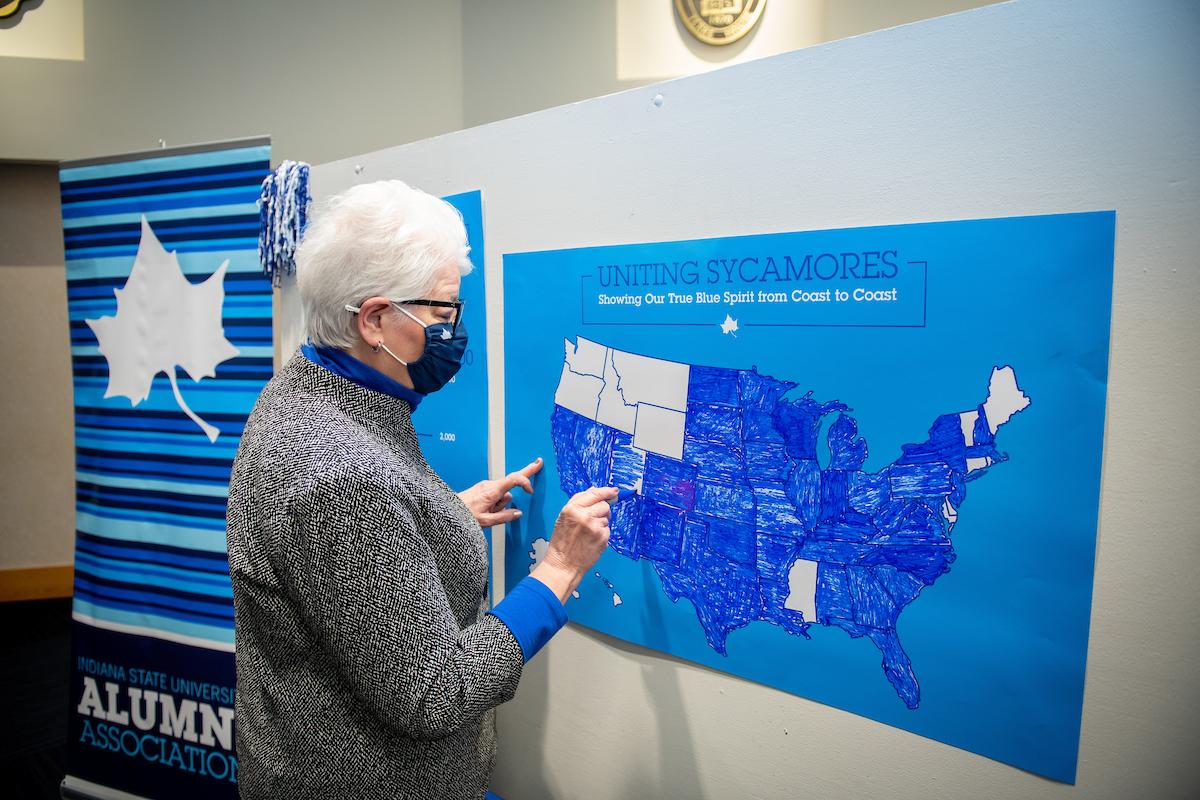 Older woman wearing a mask points to a blue map of the United States with most states filled in, signifying Indiana State University alumni reach.