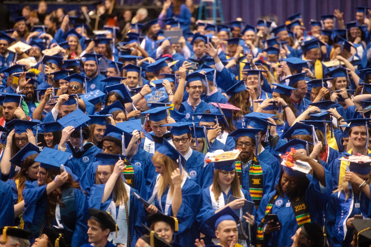 Crowd of Indiana State University graduates in blue caps and gowns gathered closely, many adjusting their mortarboards during commencement ceremony.