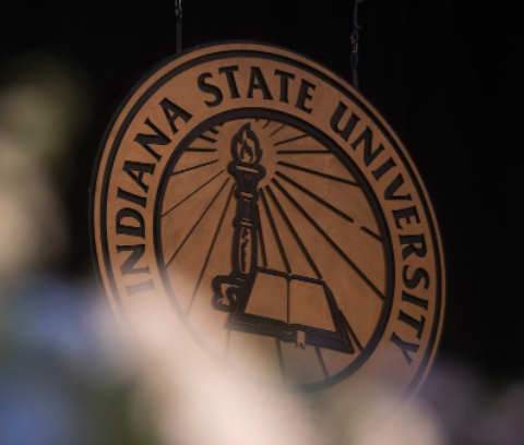 Seal of Indiana State University featuring a torch and an open book, with blurred foreground plants.