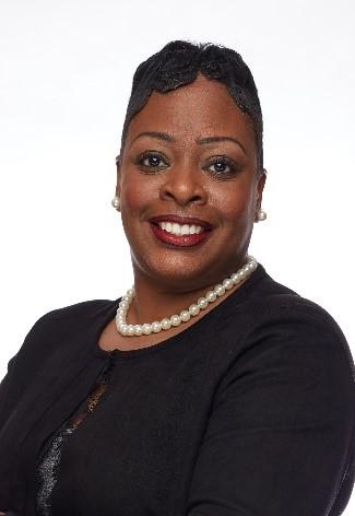 Woman with short styled hair wearing pearl earrings, pearl necklace, black jacket, smiling against white background.
