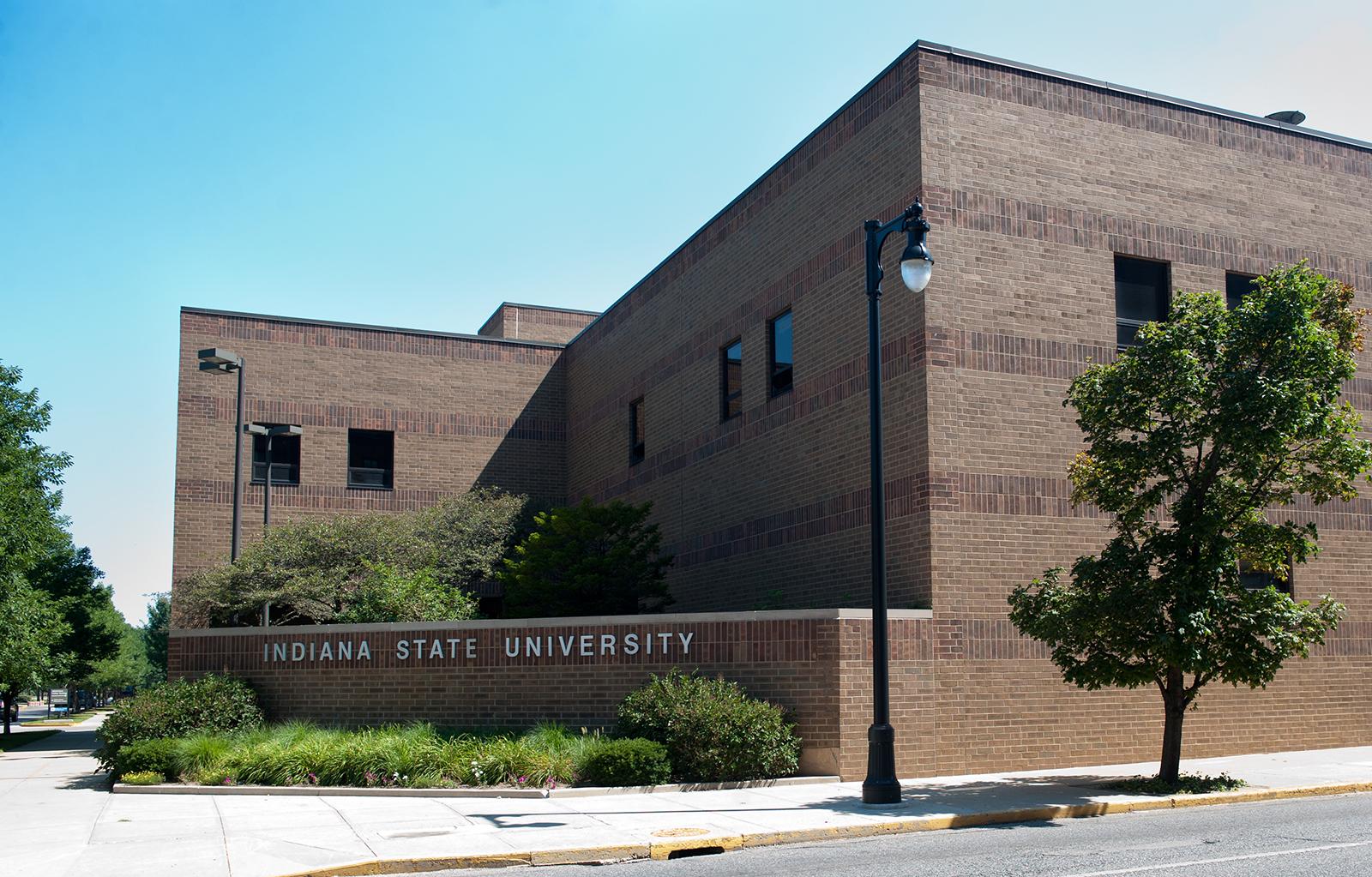 Brown brick university building with trees, a streetlamp, and Indiana State University sign on a sunny day.