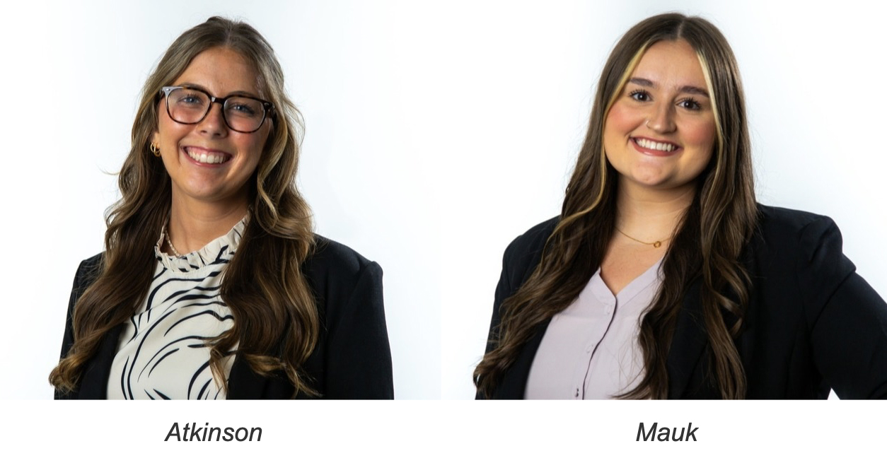 Two young women with long hair smiling against a white background, both wearing blazers over light-colored tops.