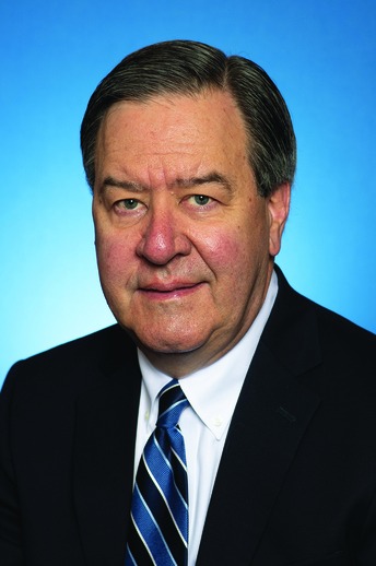 Middle-aged man with gray hair wearing a dark suit, white shirt, and blue striped tie against a blue gradient background.