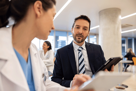 Professional in a suit holding a tablet speaks with healthcare staff in a modern office setting.